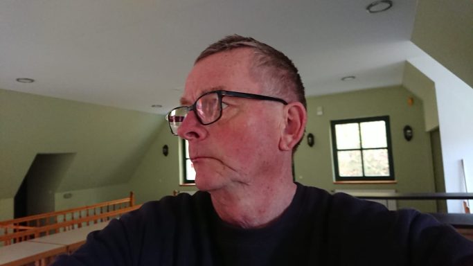 Mann mit kurzem Haar und Brille, blickt nachdenklich zur Seite in einem hellen Raum.