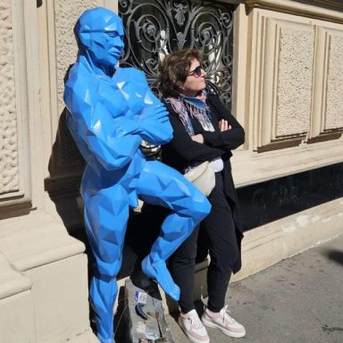 Eine Frau leans against eine blaue Statue und schaut entspannt in die Ferne.