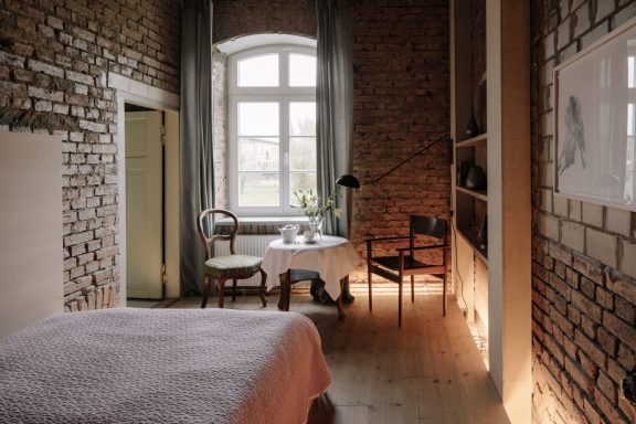 Helles Zimmer mit Backsteinwand, Tisch, Stühlen und einem Fenster mit Ausblick.
