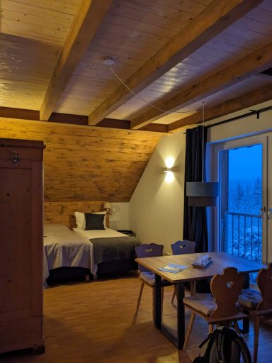 Gemütliches Zimmer mit Holzdecken, Doppelbett, Tisch und Balkon bei blauer Abenddämmerung.